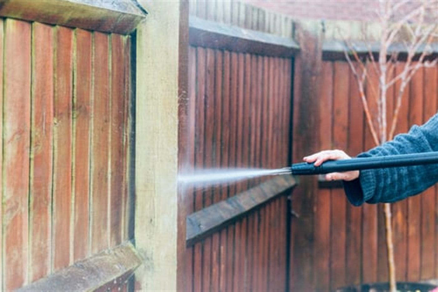 Pressure washer removing algae and grime from a weathered exterior fence, showing a clean stripe