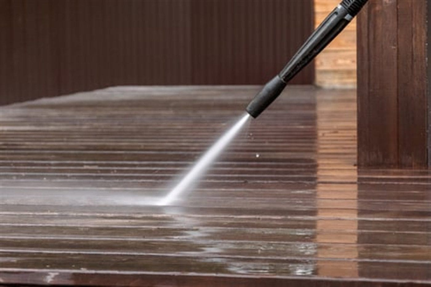 Pressure washer restoring weathered wooden deck boards, revealing clean timber beneath the grey