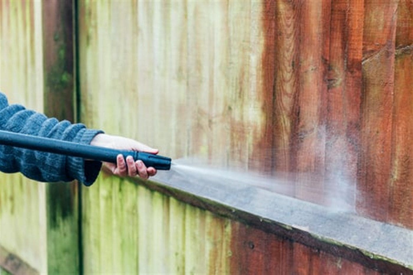 Pressure washer stripping green algae and grime from exterior house siding, showing a clean line